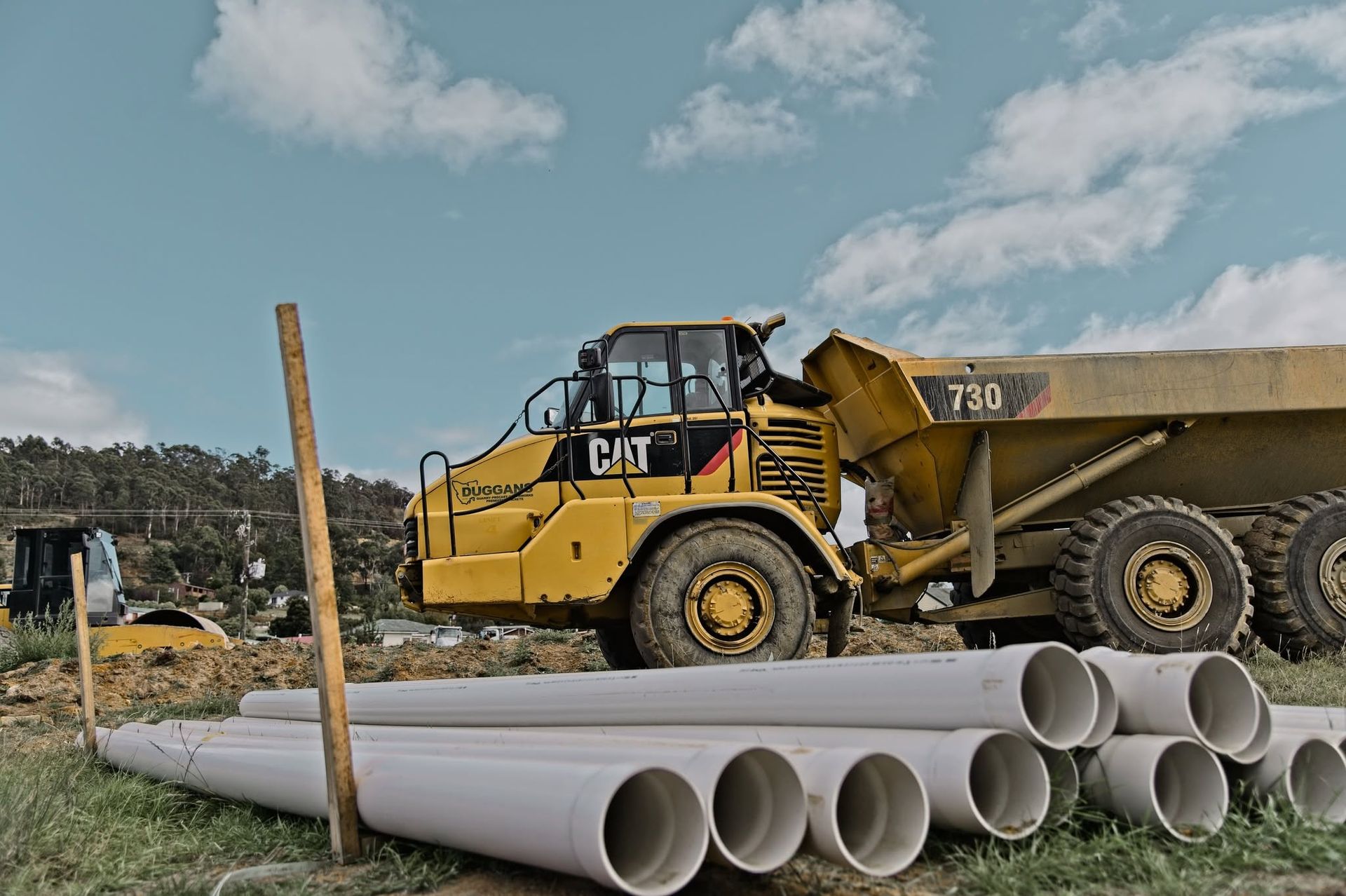 Yellow construction loader beside stacked large concrete pipes on a worksite under a cloudy sky