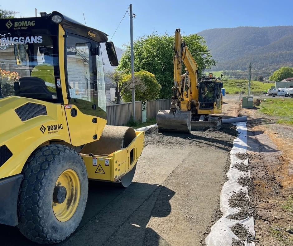 Yellow construction vehicle and excavator on a roadside with mountains in the background