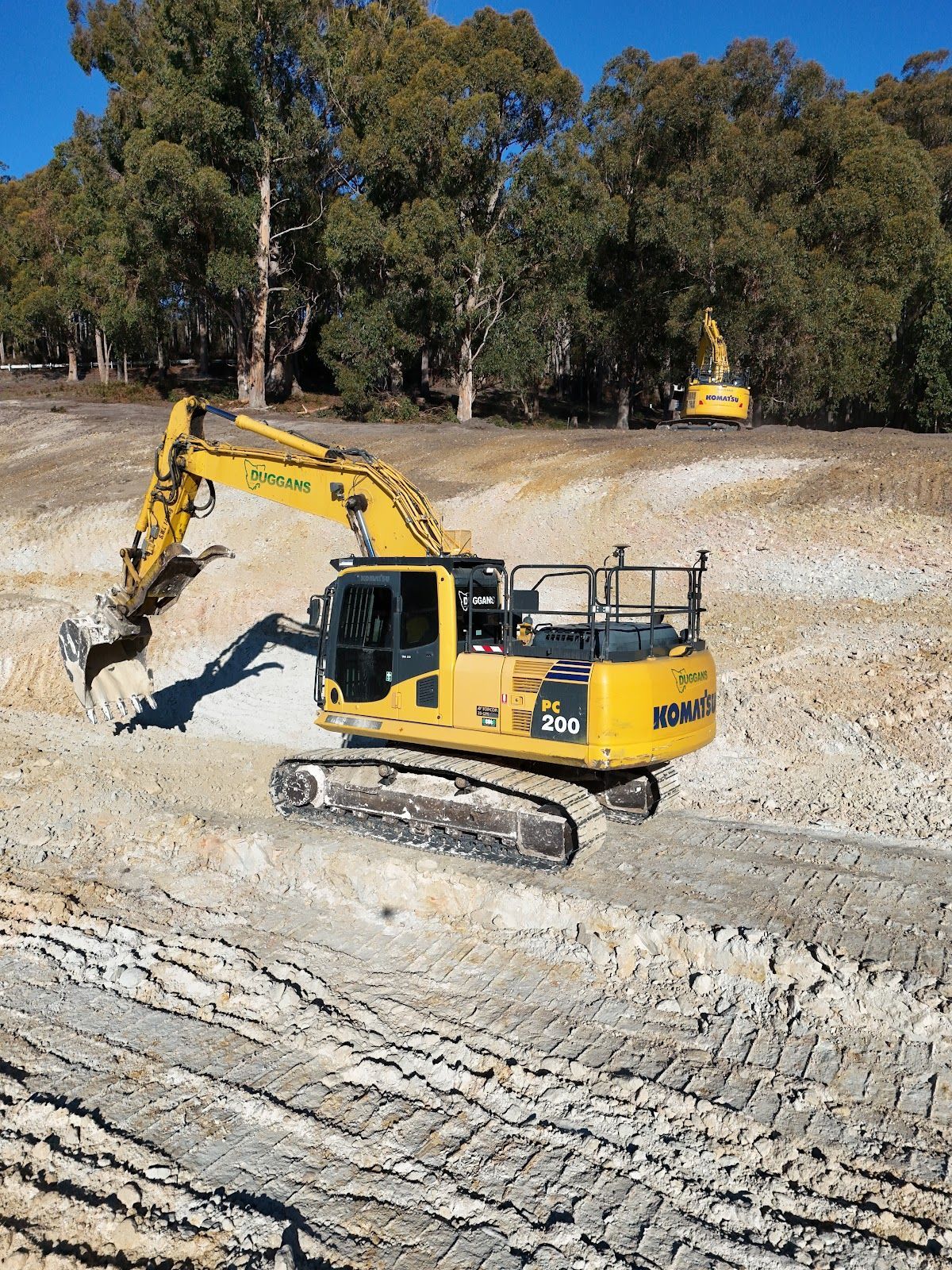 Yellow excavator loading dirt into a large industrial conveyor at a quarry