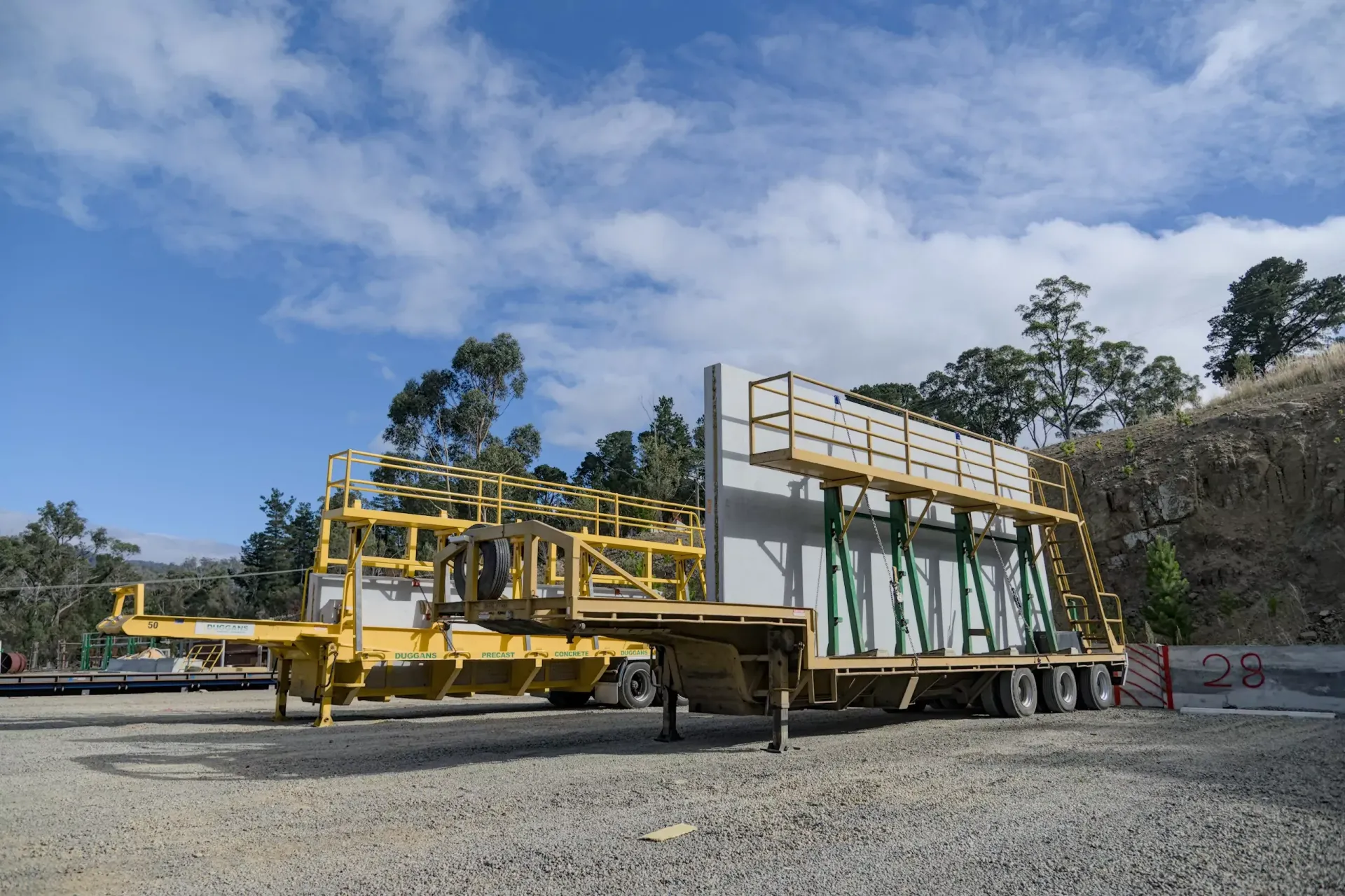 Yellow industrial machinery on a gravel lot beside a hillside under a blue sky