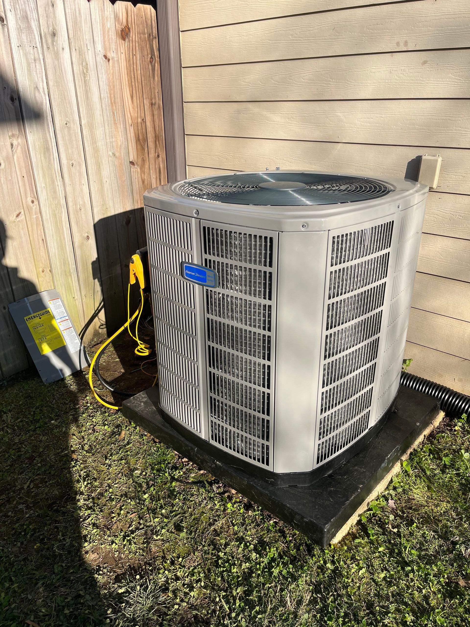 A large air conditioner is sitting on top of a black mat in the grass.