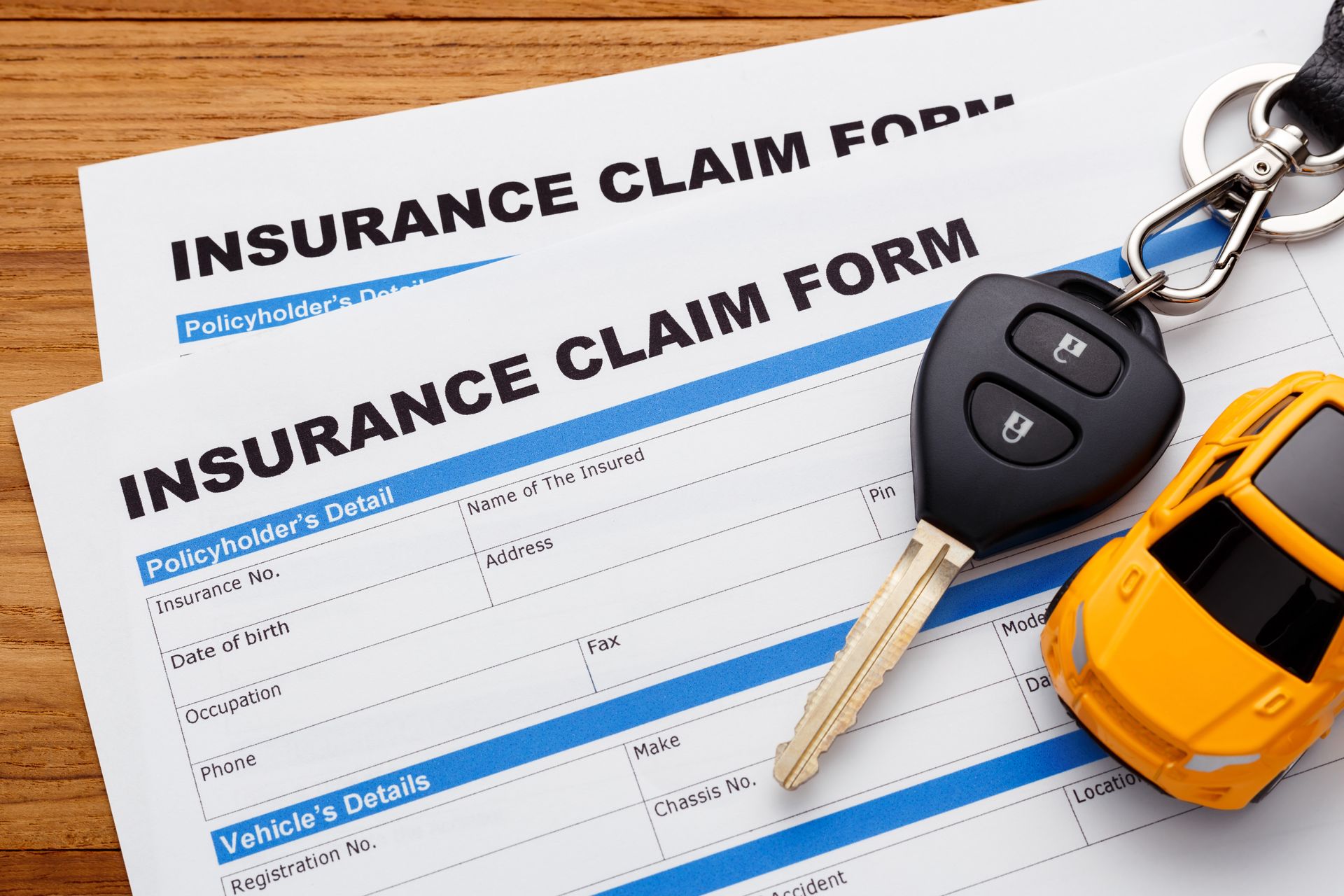 Insurance claim forms with car keys and a toy car on a wooden surface.