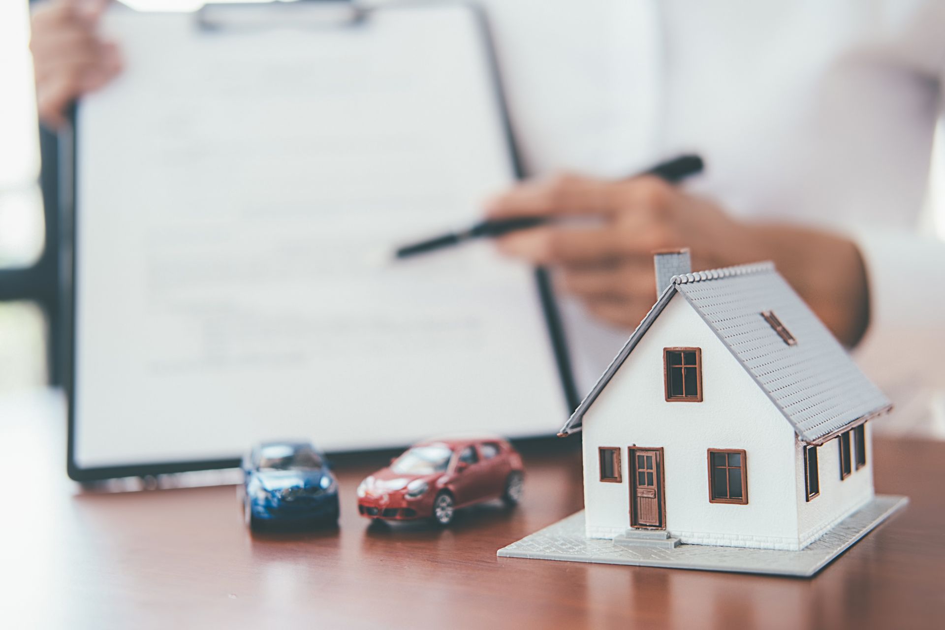 Person pointing at document, with house and car models on desk.