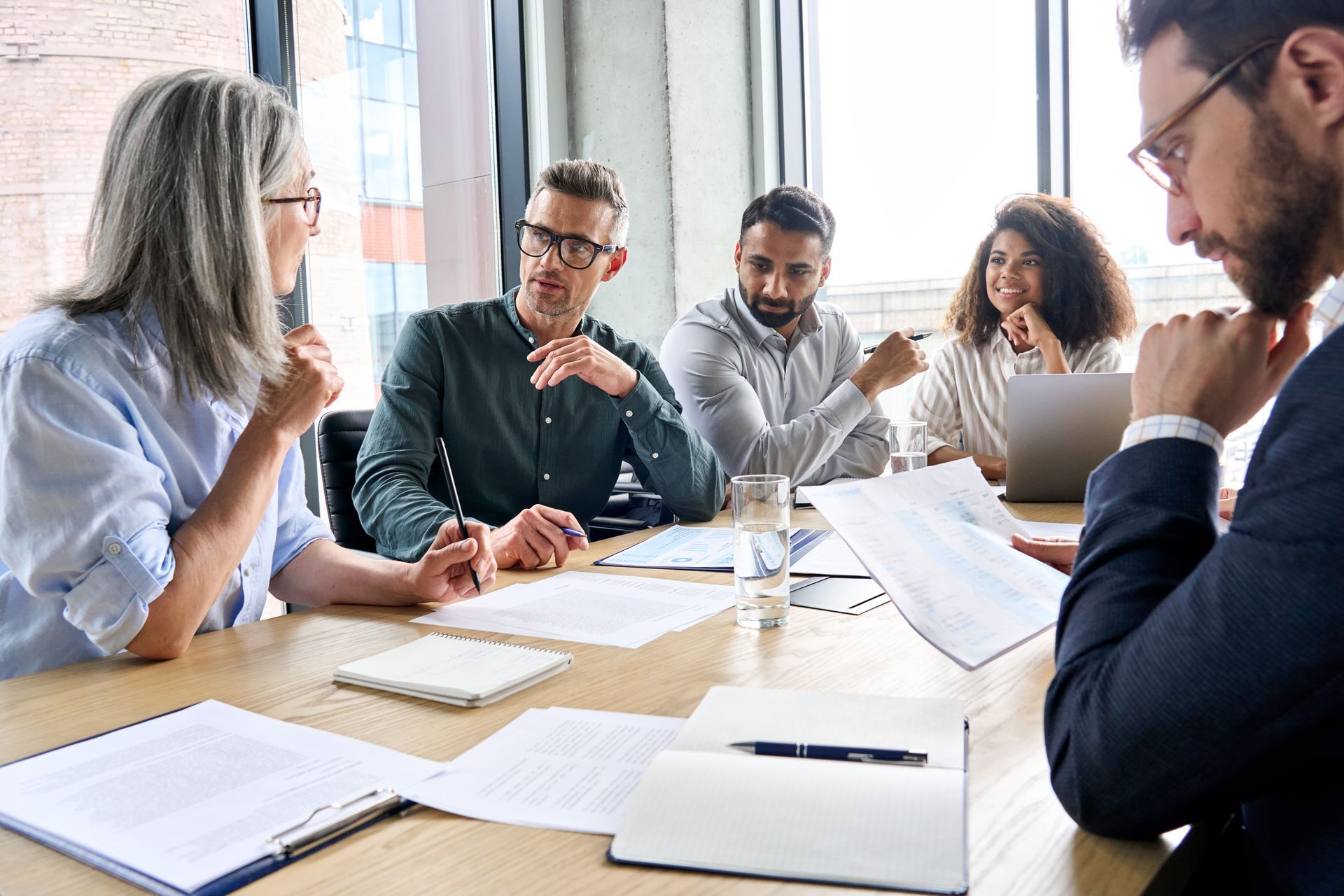 People at a table in a meeting, papers present, discussing and analyzing documents.