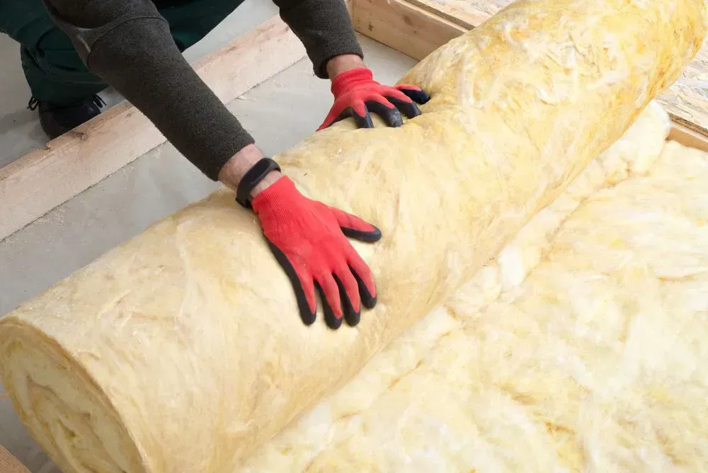 Person in Red Gloves Rolling Out Insulation in a Wooden Frame — Kev's Group QLD in Kawana, QLD