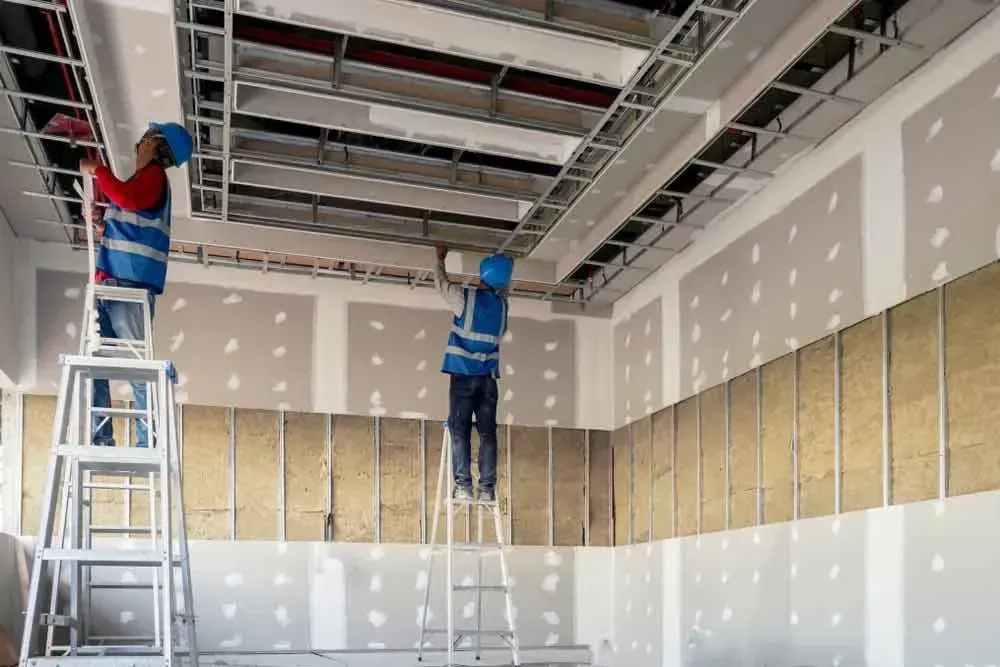 Two Construction Workers Install Ceiling Panels in a Room, Using Ladders — Kev's Group QLD in Kawana, QLD Two Construction Workers Install Ceiling Panels in a Room, Using Ladders — Kev's Group QLD in Kawana, QLD