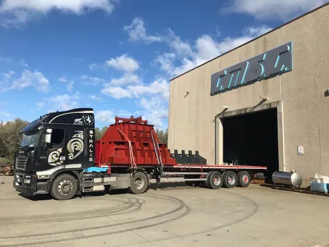 Camion con grande struttura rossa su rimorchio a pianale ribassato all'esterno di un edificio con il logo