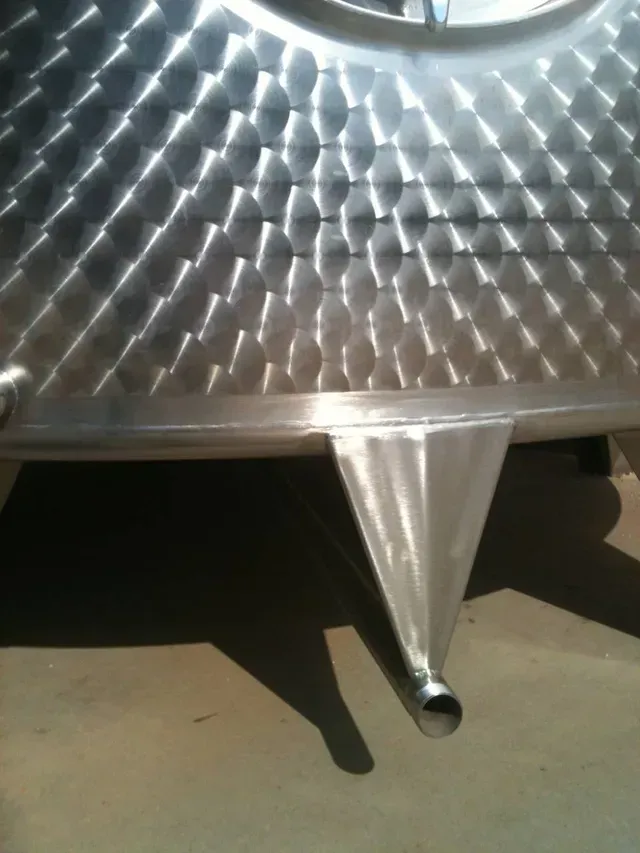 Primo piano di un serbatoio in acciaio inossidabile con superficie strutturata e fondo conico con un tubo.