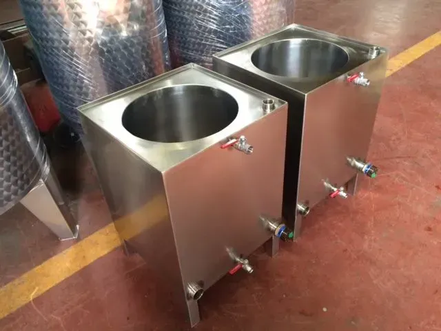 Due serbatoi rettangolari in acciaio inossidabile con aperture cilindriche, rubinetti e una botte sullo sfondo.