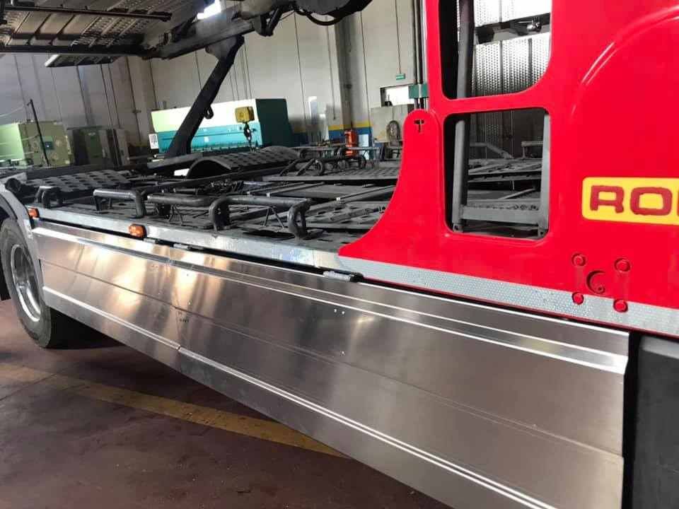 Telaio di un camion rosso e argento con meccanismo di sollevamento, probabilmente per il trasporto di container.