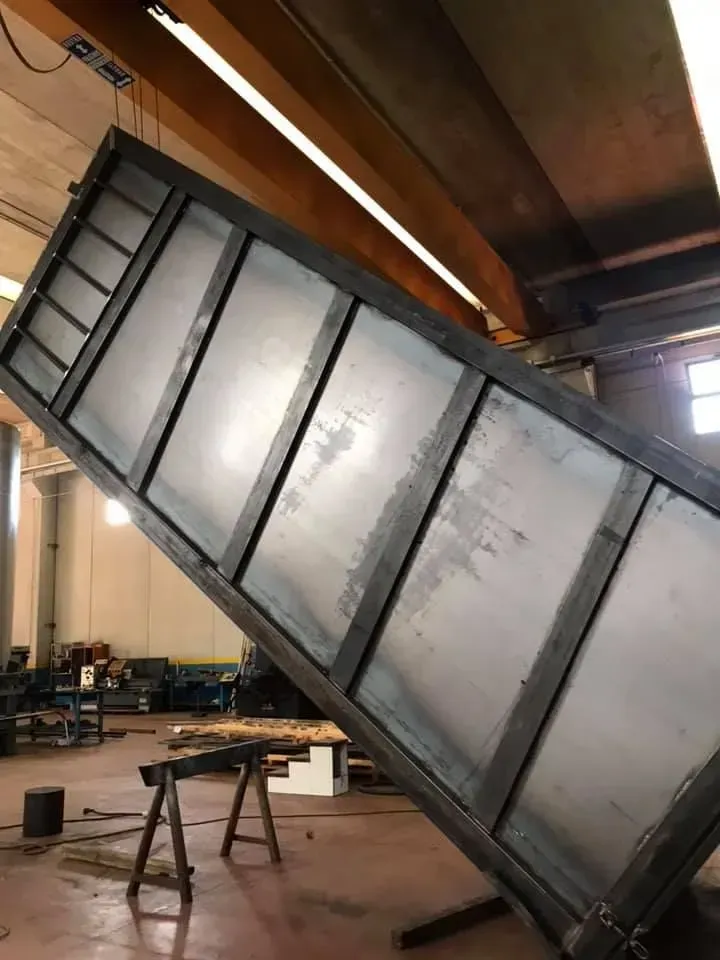 Cassone di camion in acciaio, inclinato verso l'alto in un'officina. Gru a ponte e travi a vista.