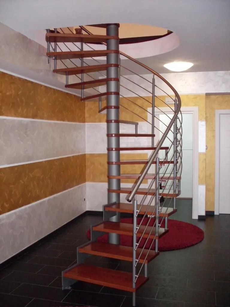 Scala a chiocciola con gradini in legno, supporti in metallo e un tappeto circolare rosso.