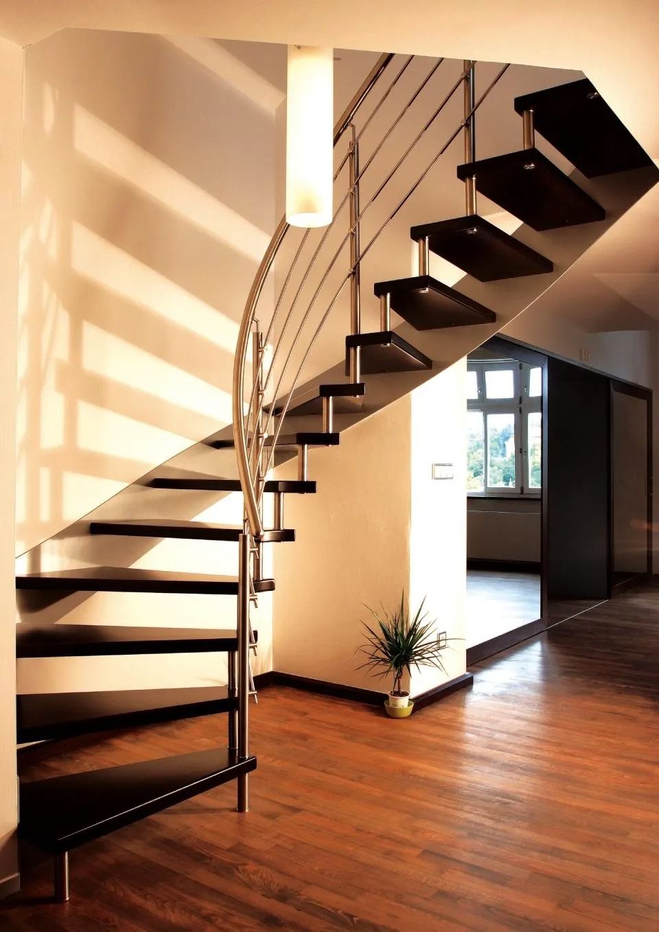 Moderna scala a chiocciola con gradini in legno scuro e ringhiera in metallo in una stanza soleggiata.