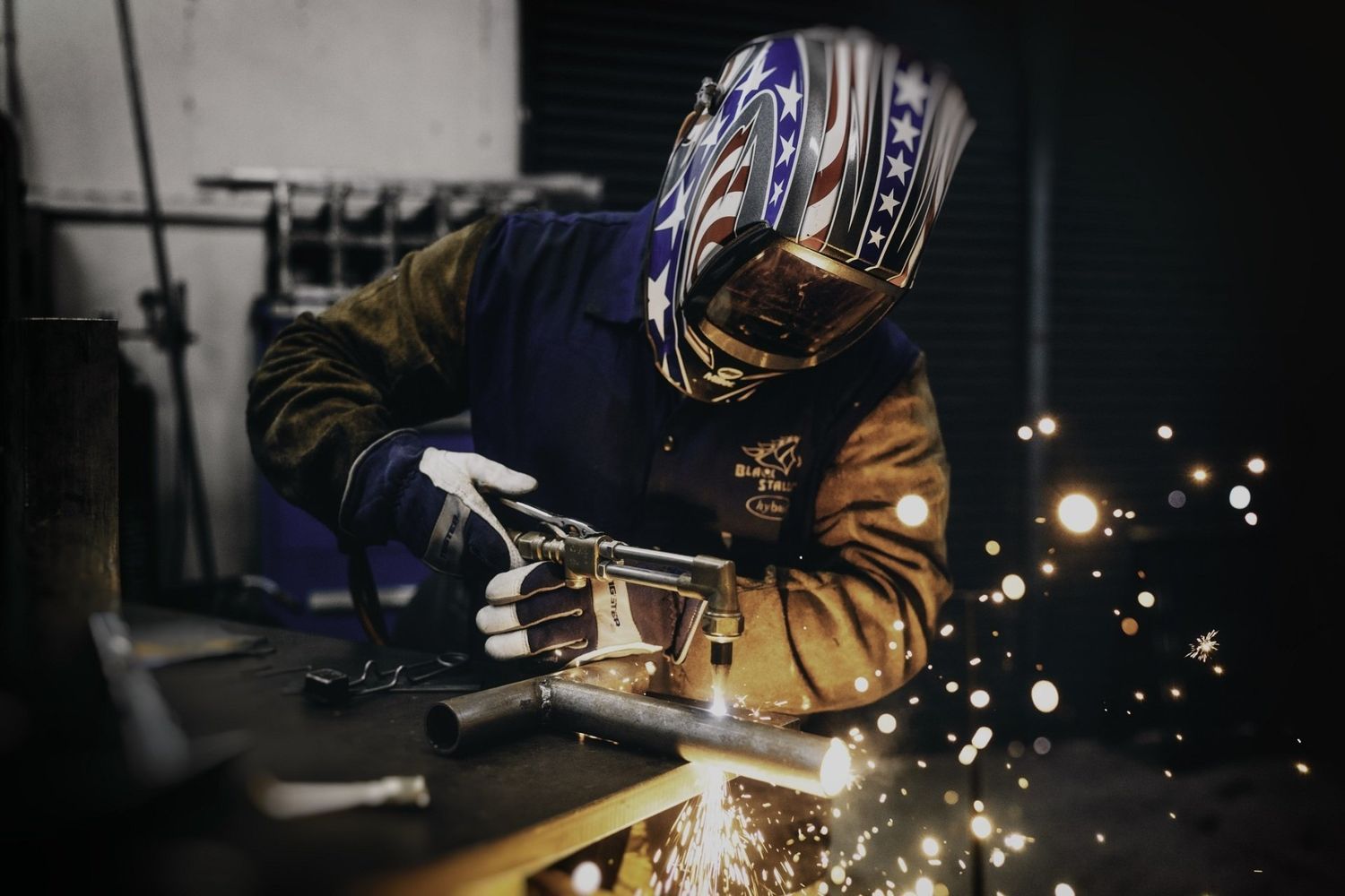 Saldatore che indossa un casco con la bandiera americana, salda il metallo in un'officina, mentre volano scintille.