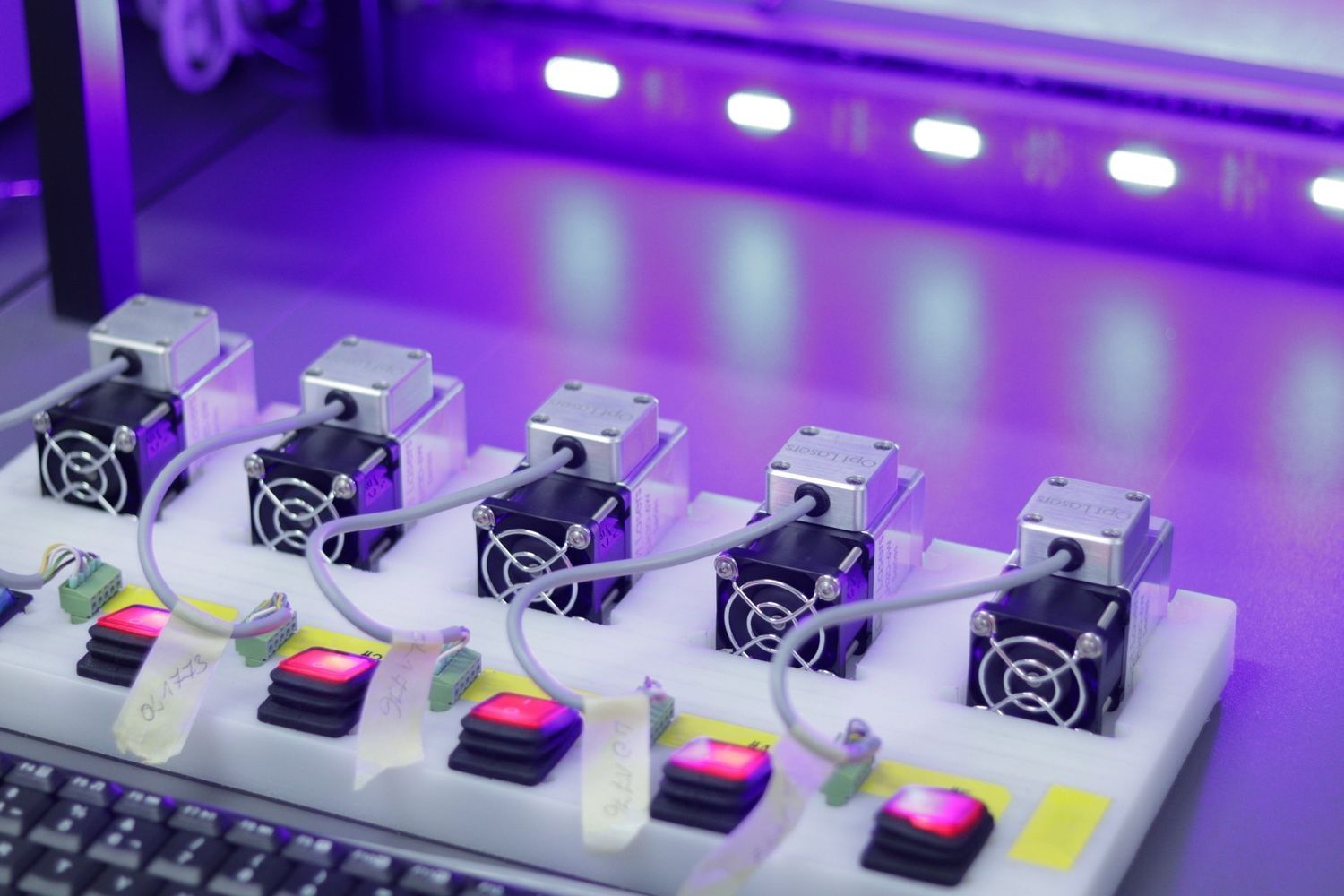 Piattaforma bianca con sei piccoli ventilatori, oggetti rossi e bianchi, illuminati da LED viola.