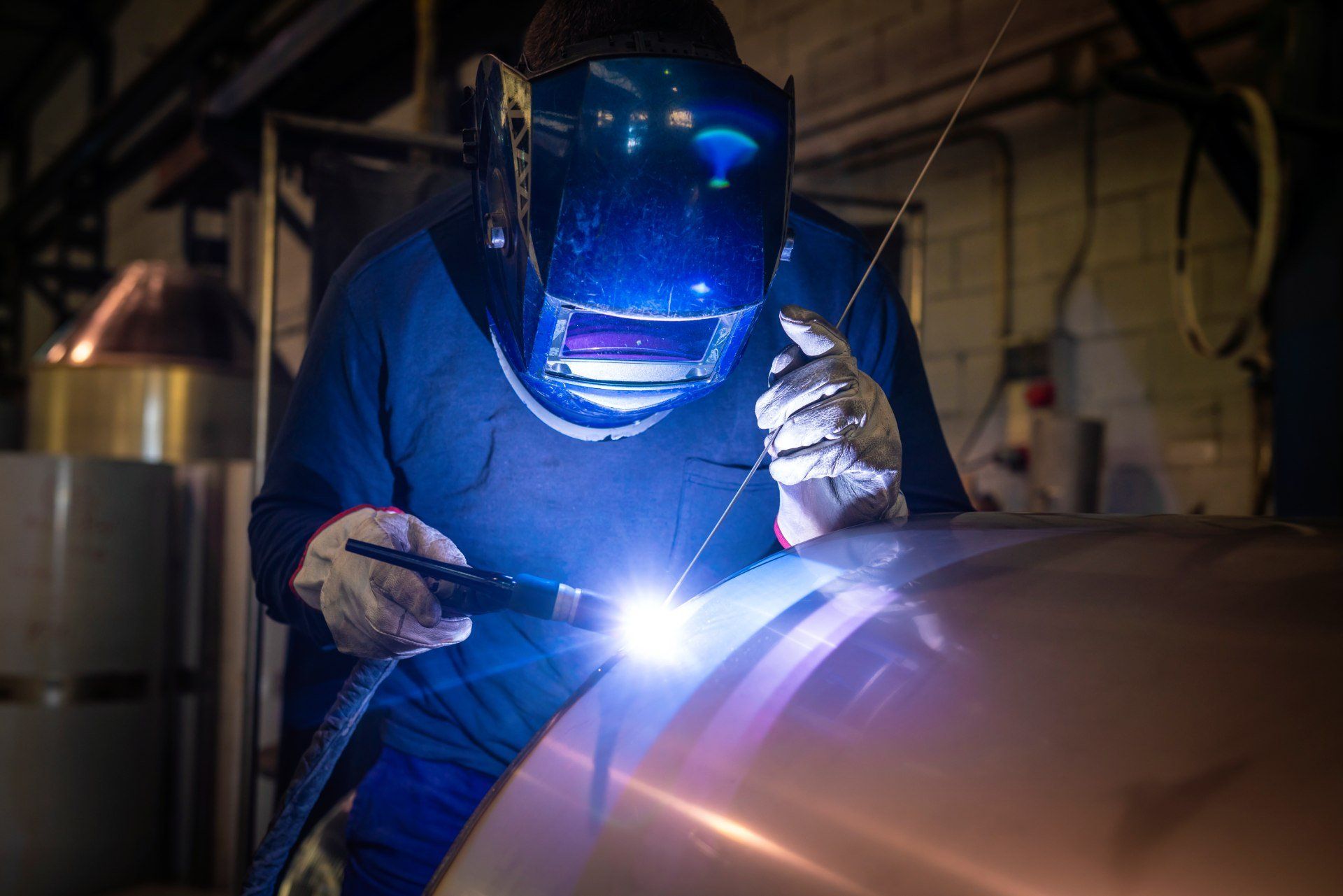 Quattro grandi serbatoi industriali in acciaio inossidabile all'interno di una fabbrica con tubi, valvole.