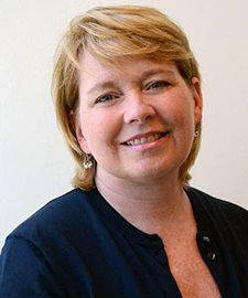 Smiling woman with short blonde hair in a dark top against a light background