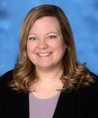 Smiling woman in a black blazer and lavender top against a blue studio backdrop