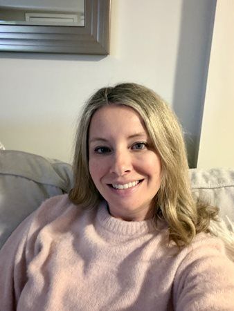Smiling woman in a light pink sweater sitting on a couch in a living room