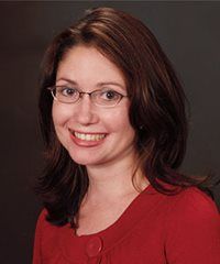 Portrait of a smiling woman with glasses in a red top against a dark background