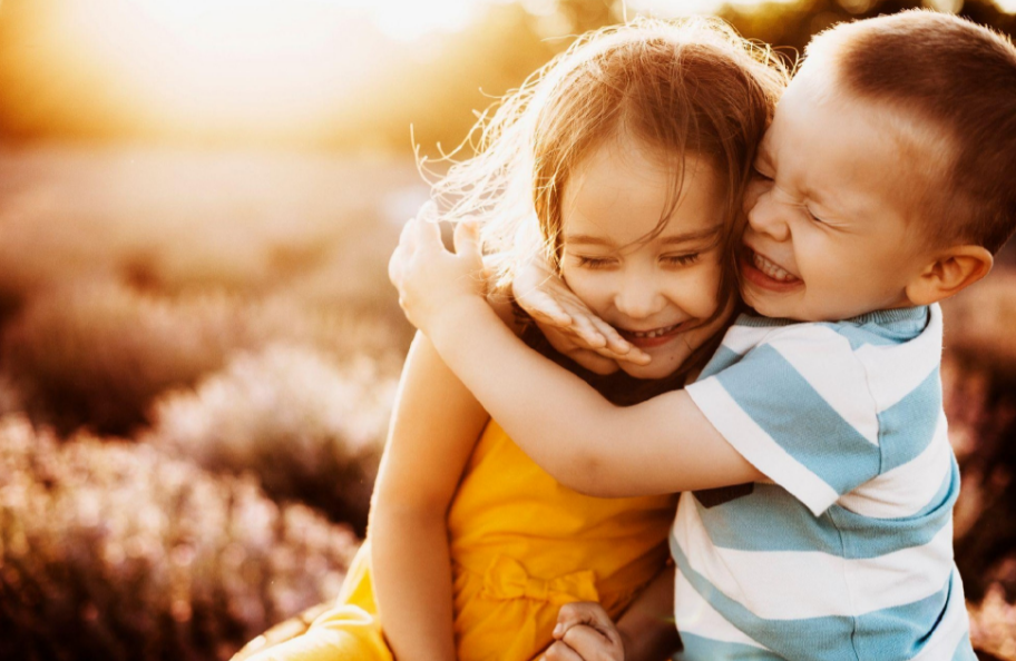 Two children hugging in a sunny field, one in yellow and one in a striped shirt