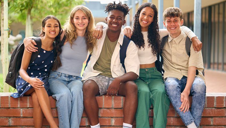 Five friends sitting on a brick ledge outdoors, smiling at the camera.