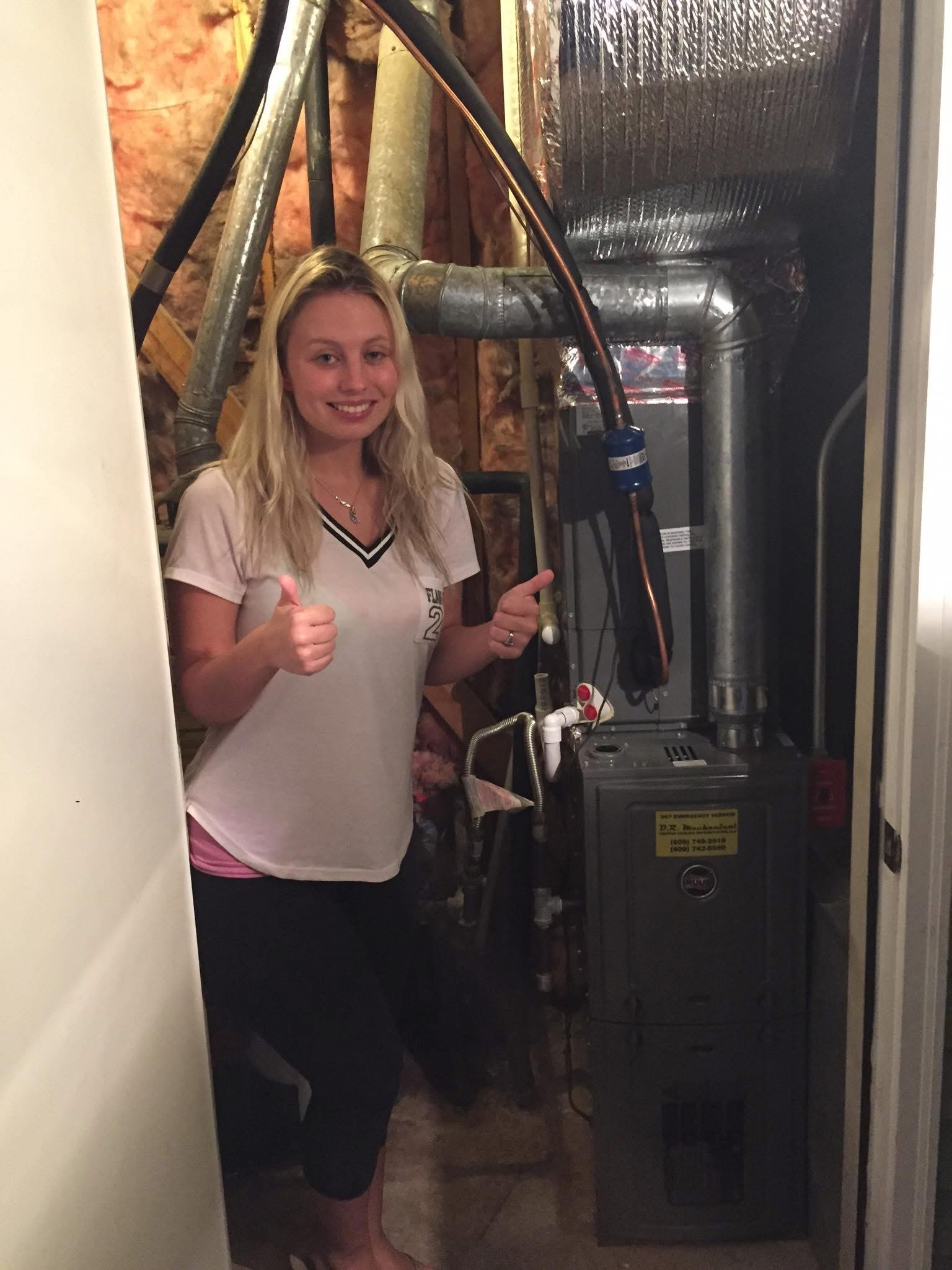 Woman giving thumbs-up in a narrow utility room beside HVAC equipment and pipes