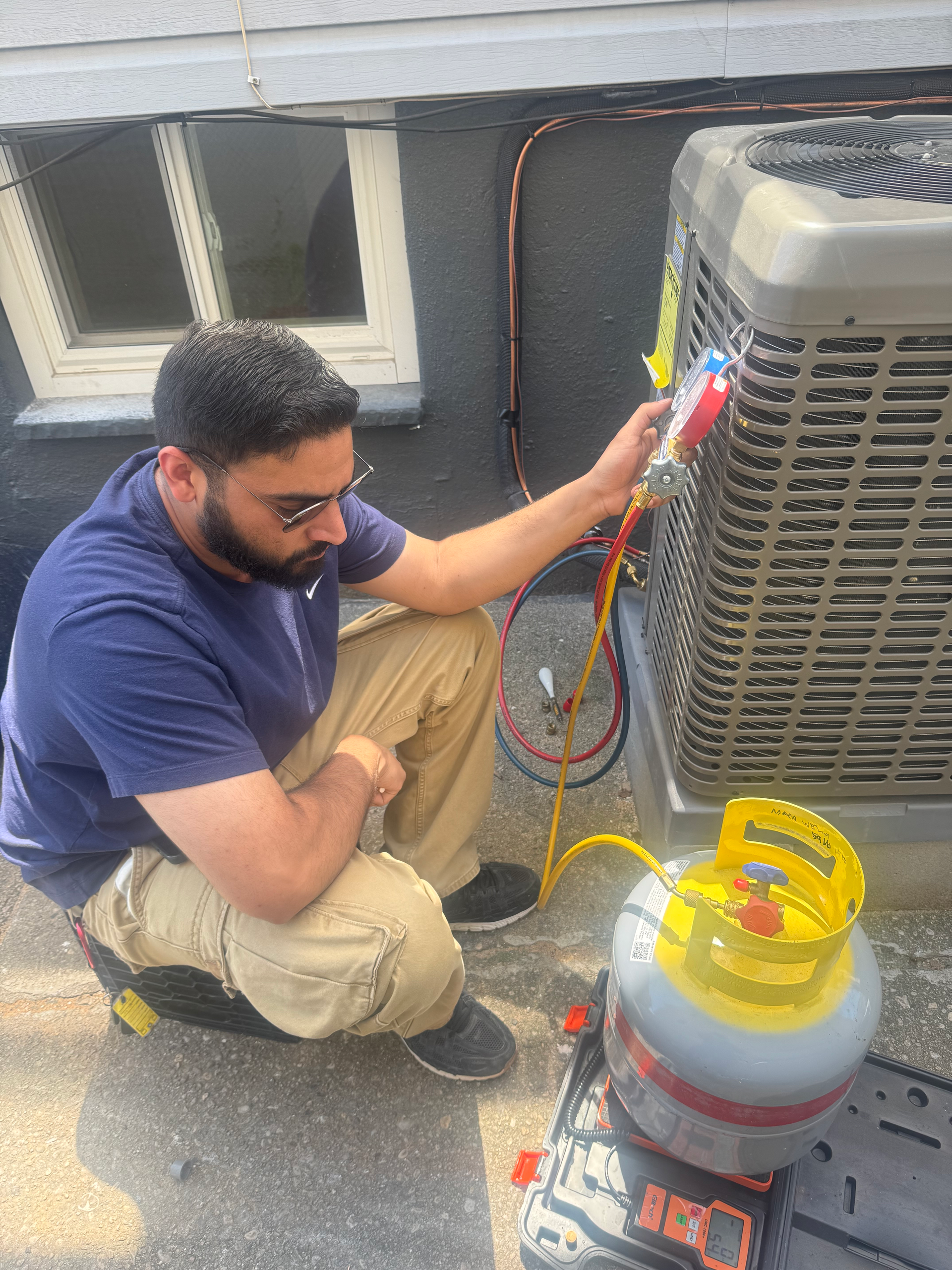 Technician checking rooftop HVAC unit with gauges and hoses beside a gas cylinder