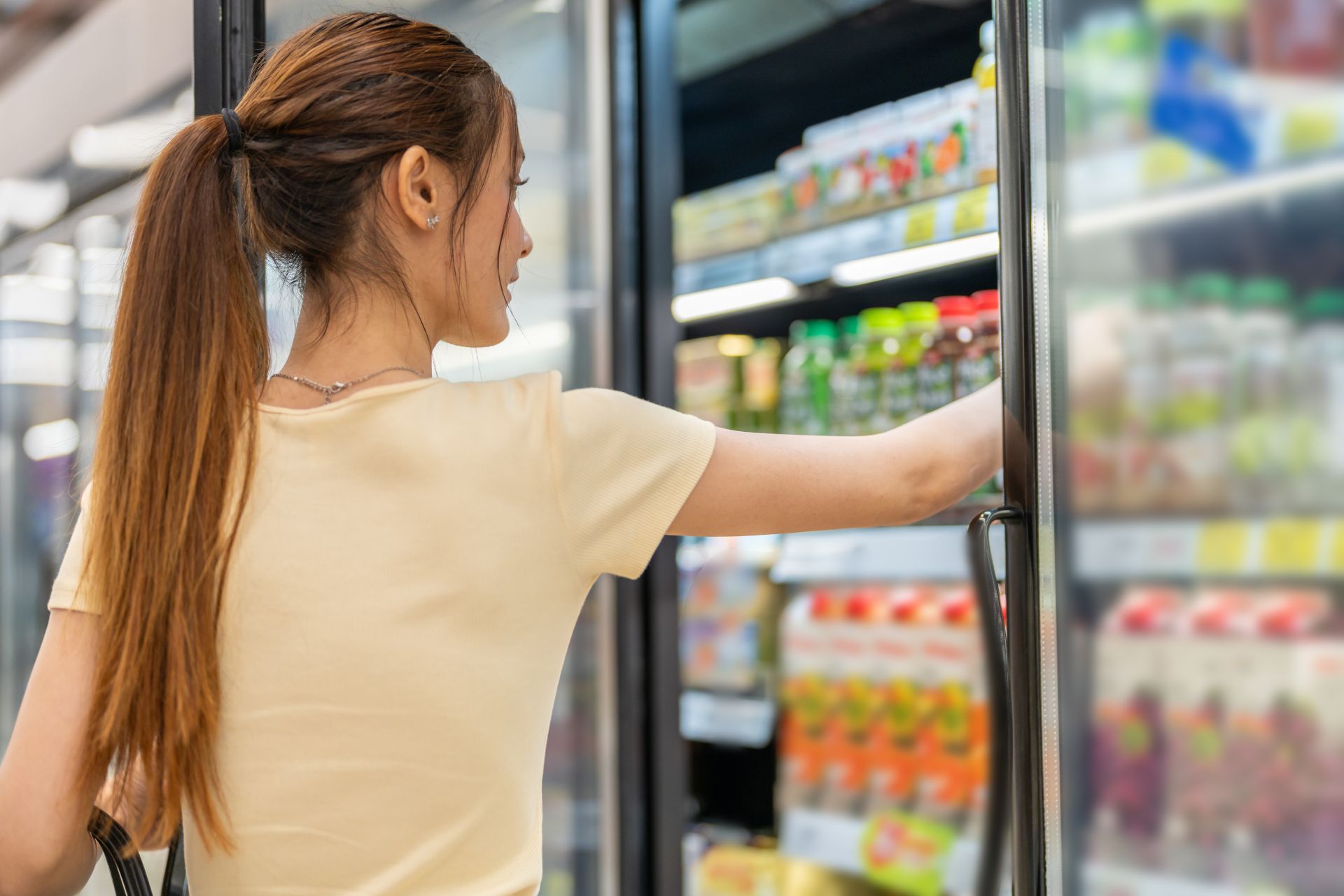 Woman selecting a drink from a refrigerated store shelf.