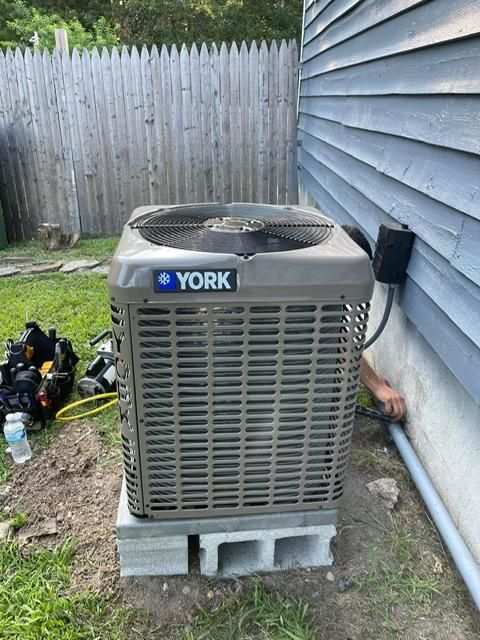 York HVAC unit on concrete blocks beside a house, with a fenced backyard and yard tools nearby
