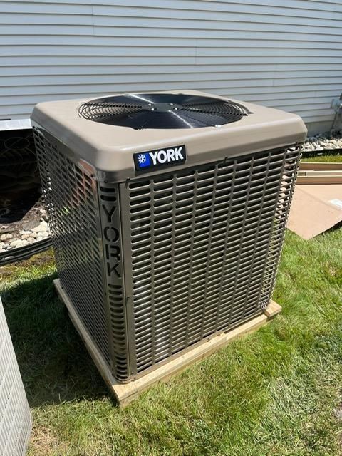 York outdoor air conditioner unit on grass beside a house, with a beige cover and top fan.