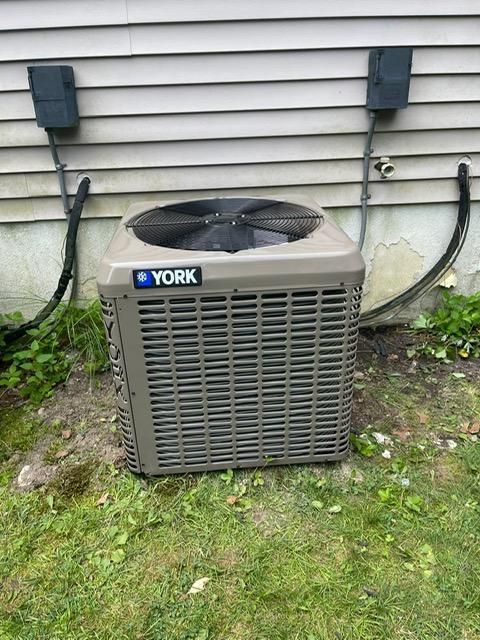Outdoor York air conditioner unit beside a house with gray siding and grass around it