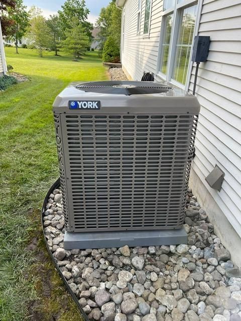 York outdoor AC unit beside a house, set on a gravel bed beside a lawn.