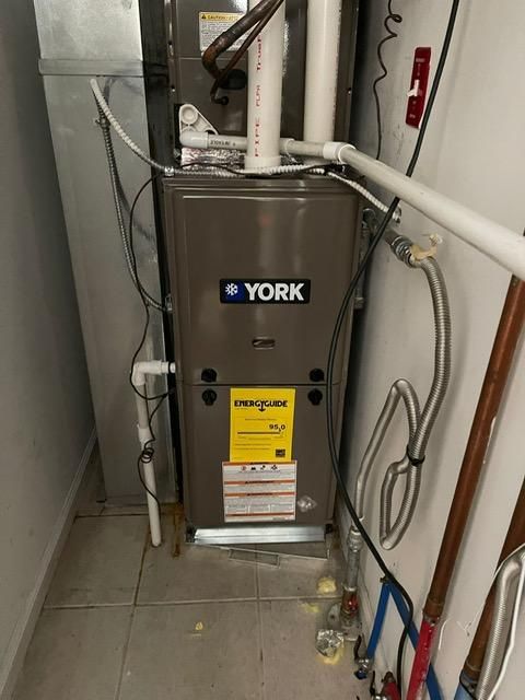 York furnace unit in a utility closet with exposed pipes and hoses.