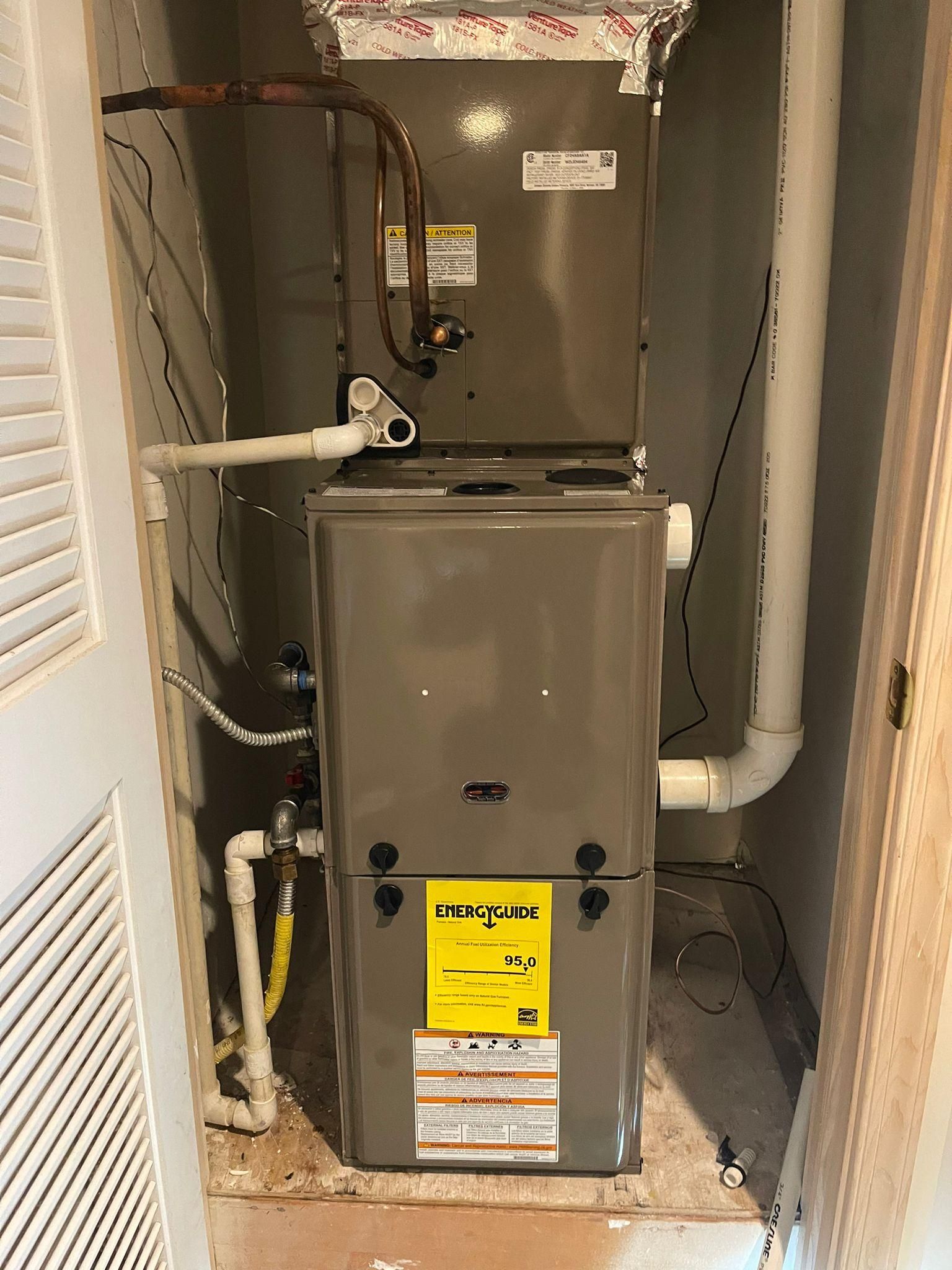 Furnace and HVAC equipment in a narrow utility closet with exposed pipes and ducts.