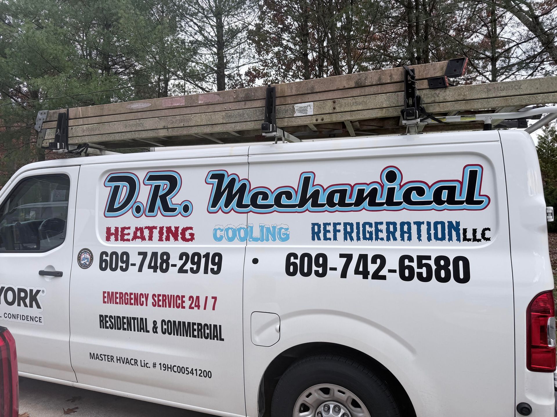 White D.R. Mechanical HVAC van with phone numbers parked outdoors under a wooden fence.