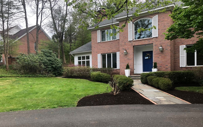 Brick house with white trim, green lawn, and wet driveway on a cloudy day