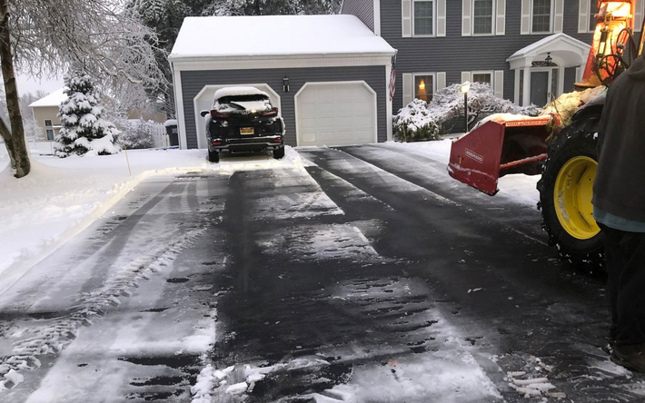 Snowy driveway with a red car cover, leading to a garage and house in winter.
