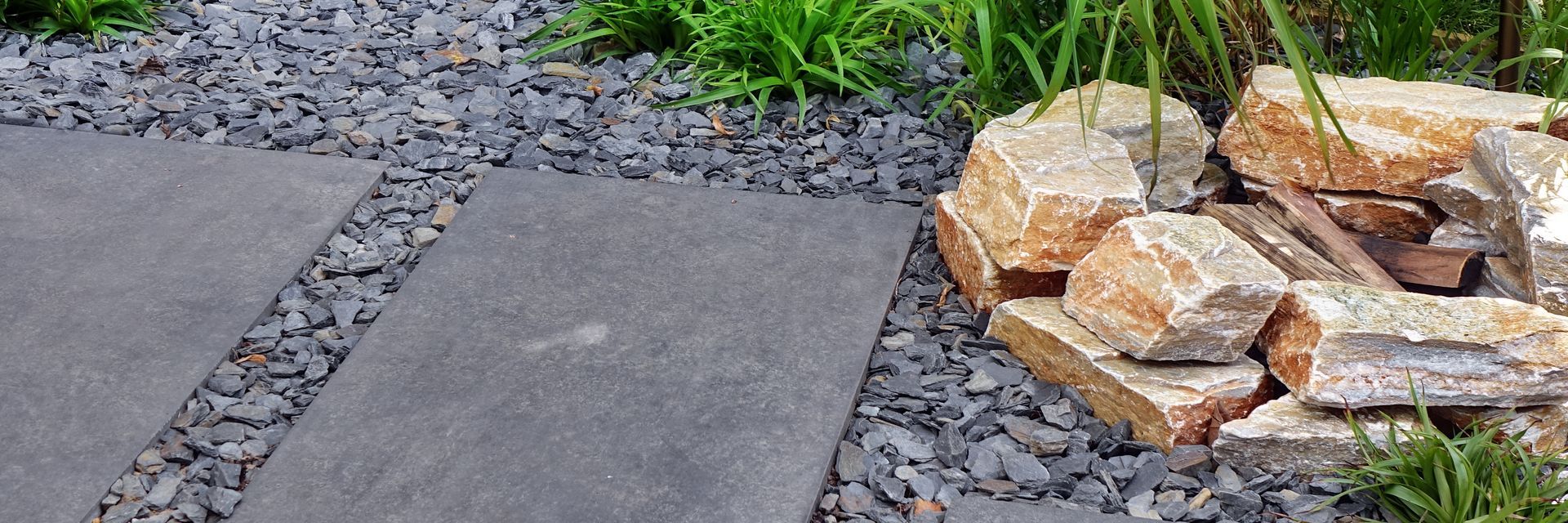 Paved stepping stones beside gray gravel and a stack of tan rocks in a garden