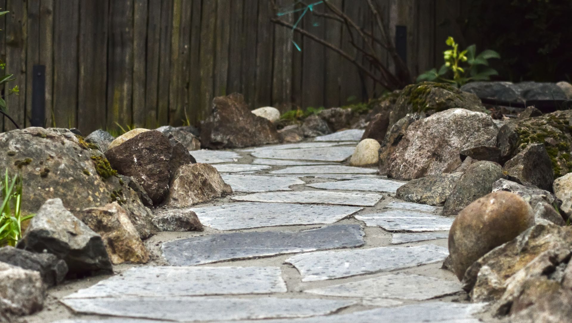 Stone garden path winding uphill between rocks and a wooden fence.
