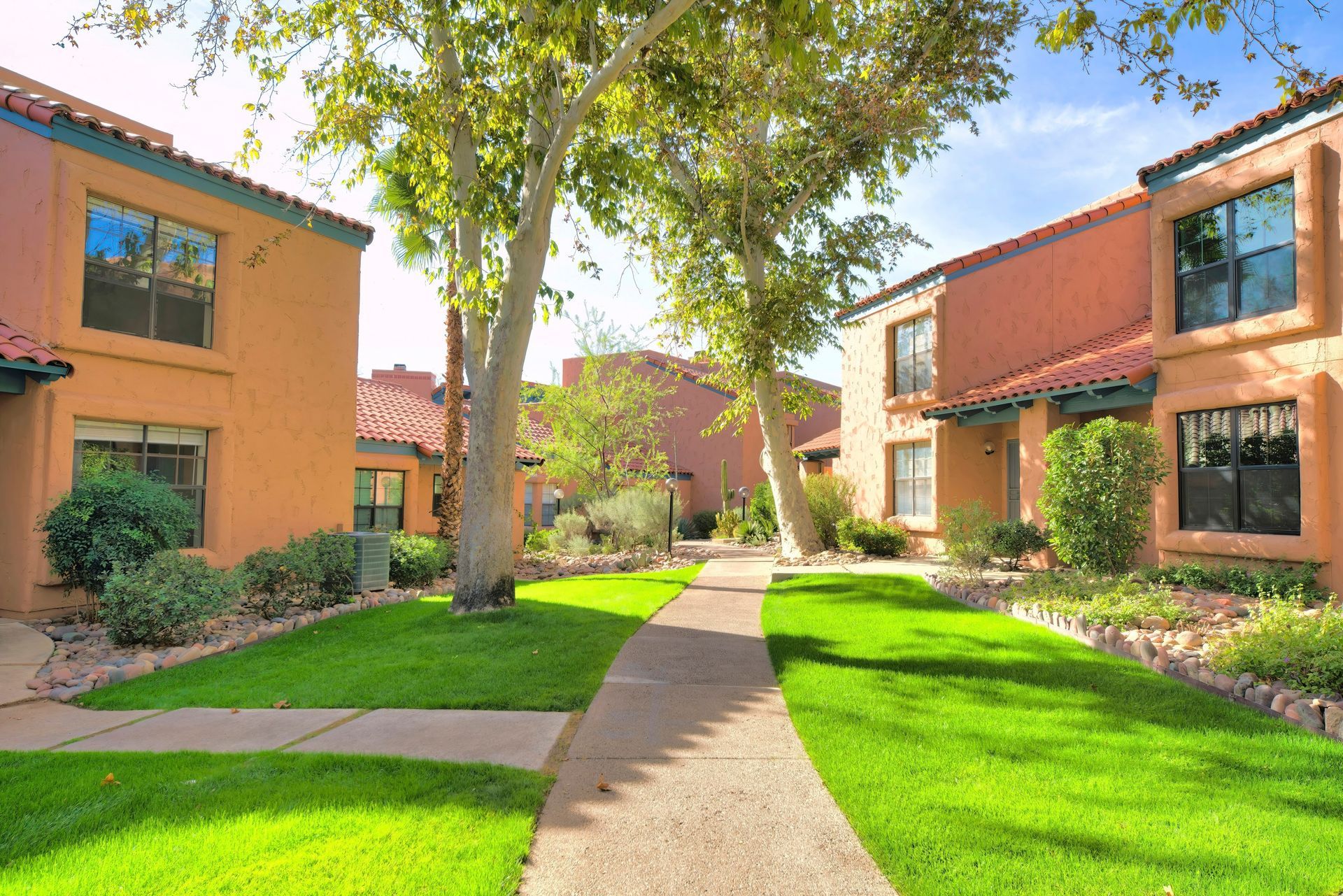 Courtyard between orange apartment buildings with green lawn, trees, and a winding sidewalk