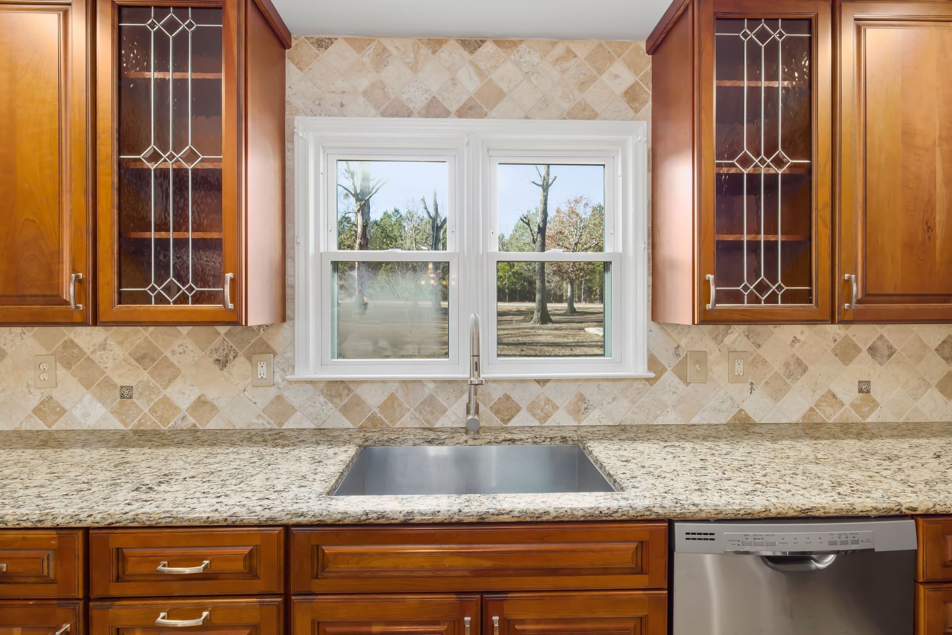 Modern kitchen sink with chrome faucet, gray tile backsplash, and wood cabinet front