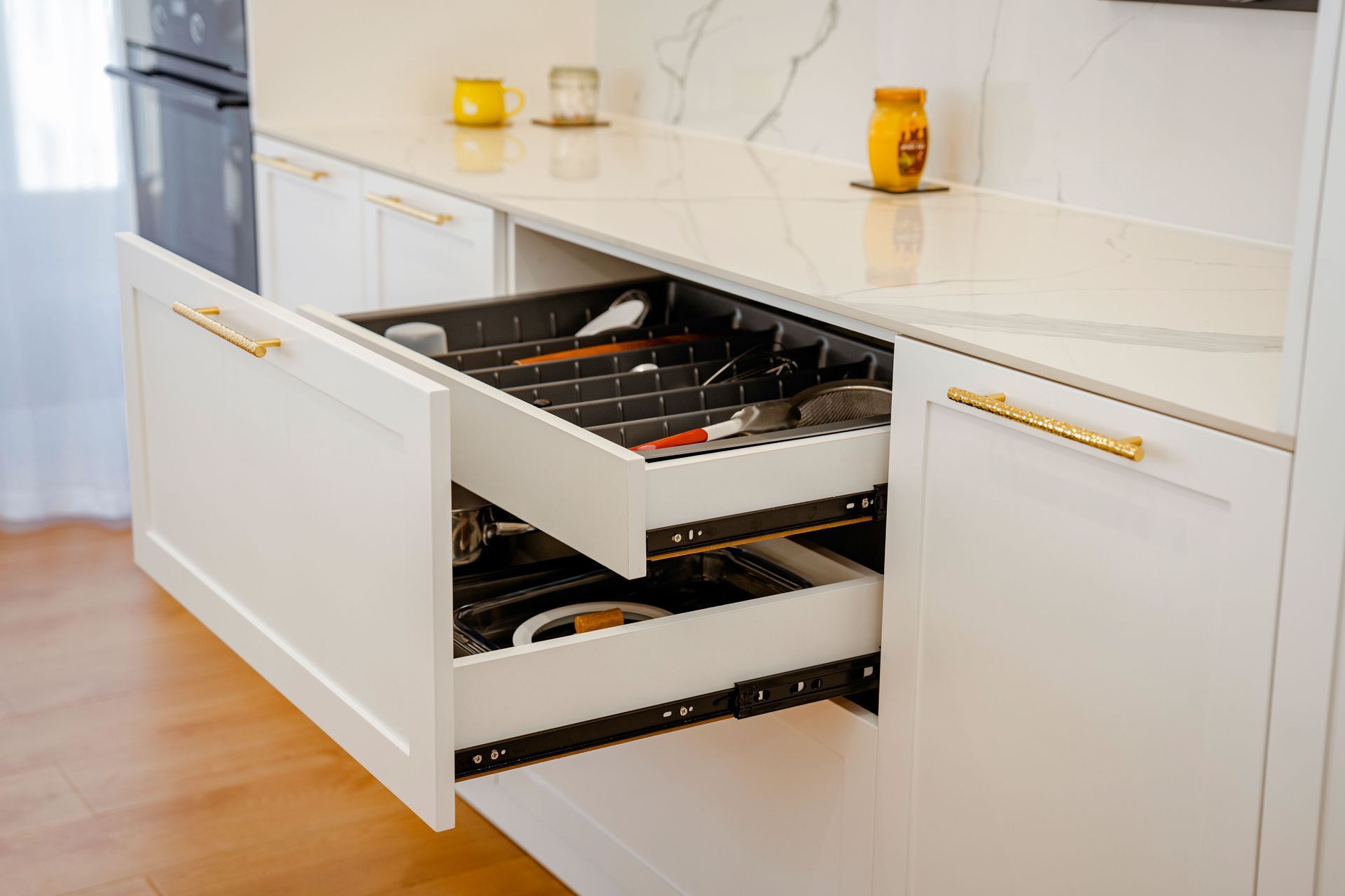 White kitchen drawer open with organized cutlery and utensils beneath a countertop