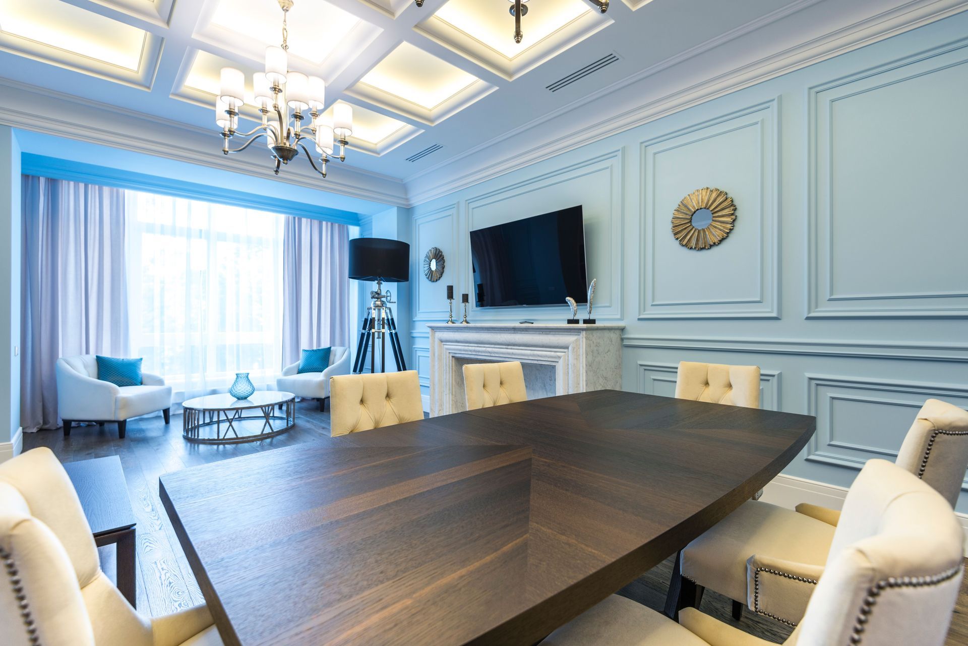 Elegant blue dining room with a dark wood table, cream chairs, chandelier, and wall-mounted TV.