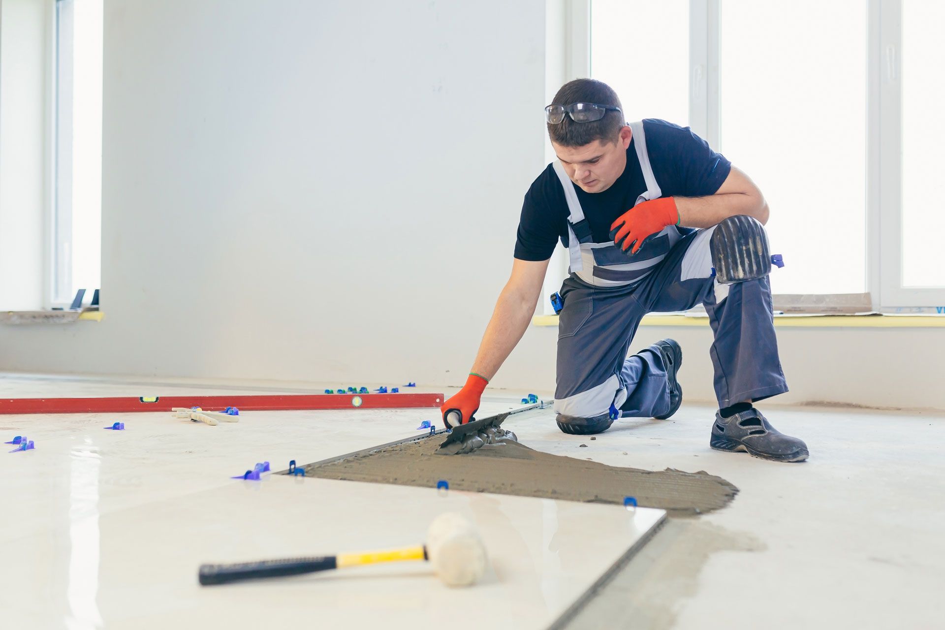 Worker kneeling and applying flooring adhesive in a bright room with tools nearby