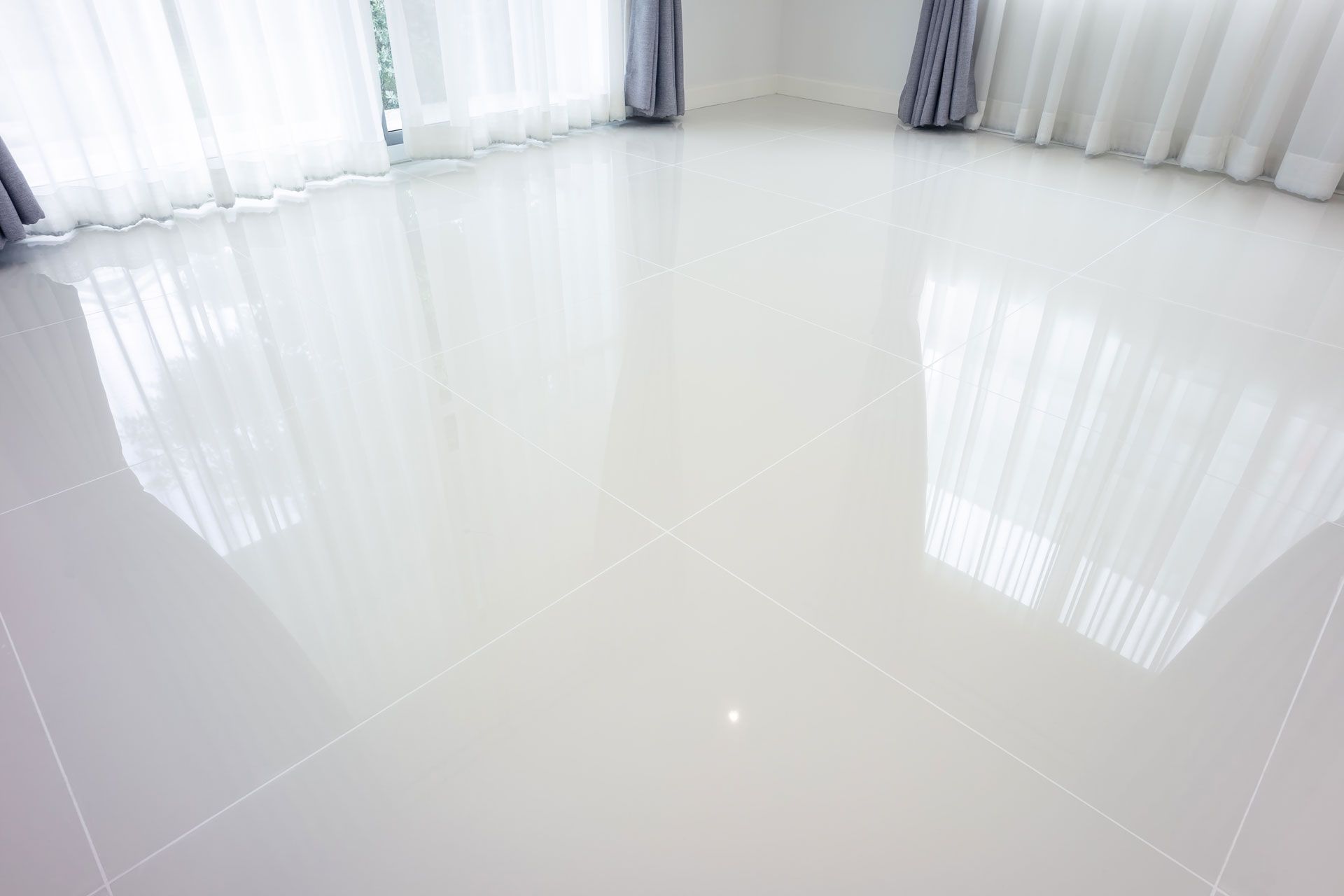 Glossy white tiled floor in a bright room with sheer curtains along the walls