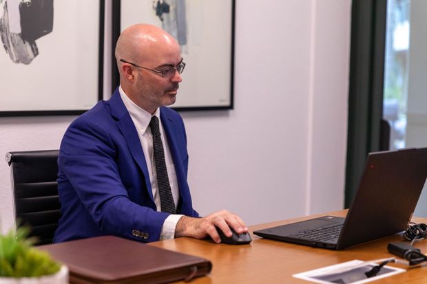 Man in a blue suit working on a laptop at a desk in an office