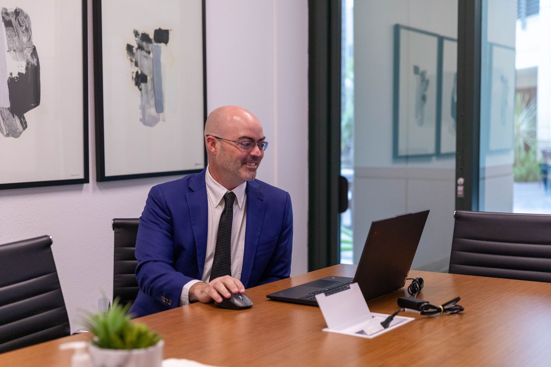 Man in blue suit working at a conference table in a modern office with a laptop and papers