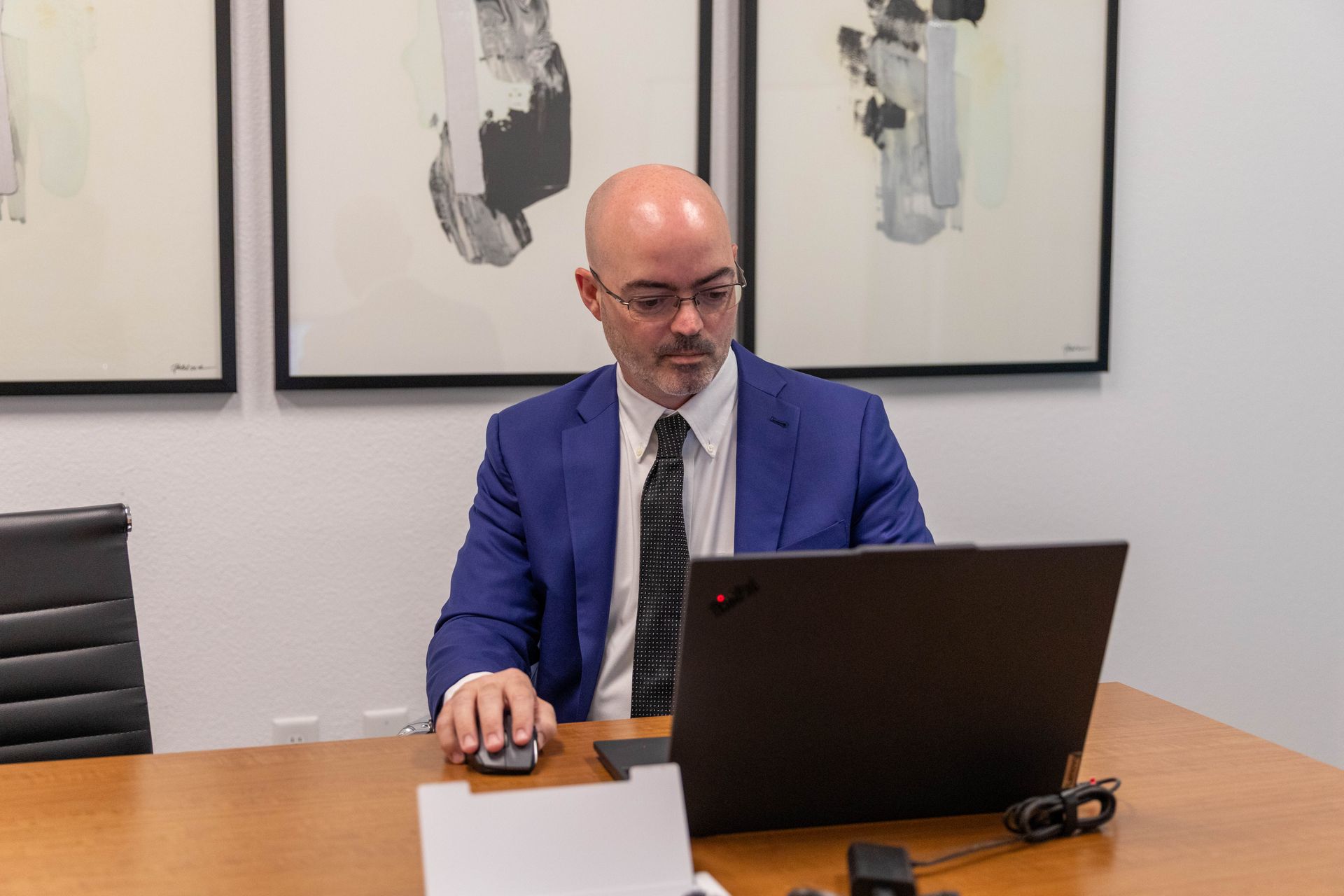 Man in a blue suit working on a laptop at a conference table in an office.