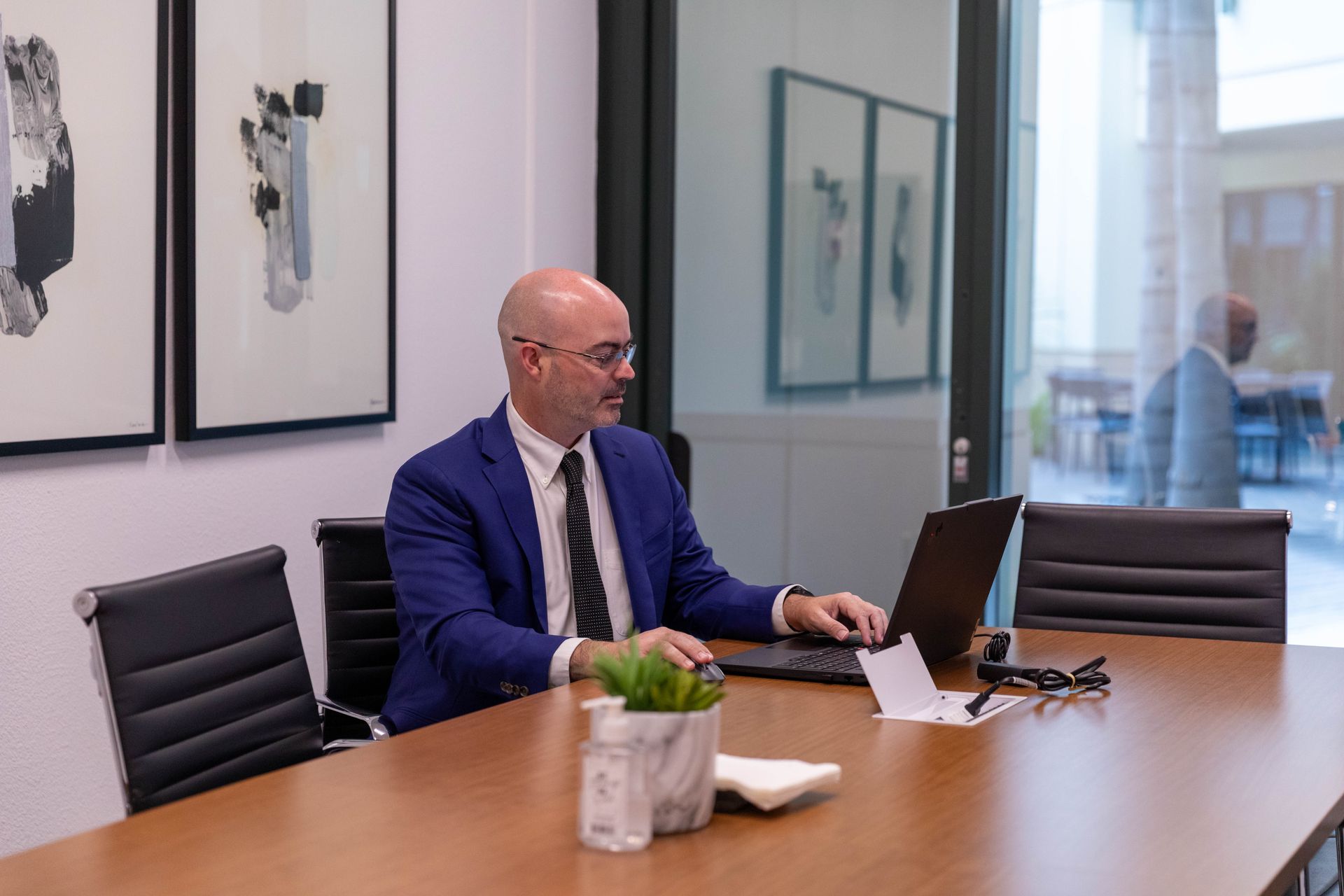 Man in a blue suit working on a laptop at a conference table in a modern office